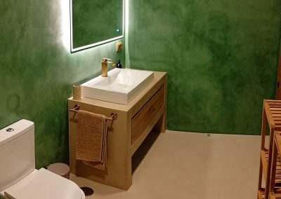 Baño de microcemento verde con grifería dorada