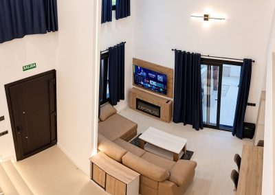 Salón de doble altura con sofá, chimenea y salida al jardín